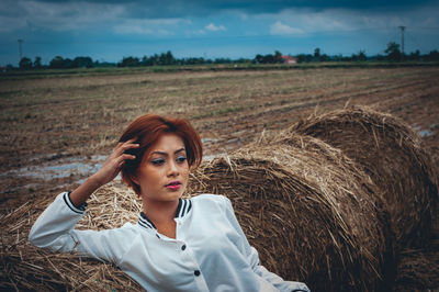 Thoughtful woman sitting on hay bale at field