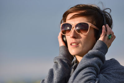 Close-up of mid adult woman wearing sunglasses while listening music against clear sky