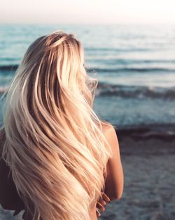 Rear view of shirtless woman with long hair at beach