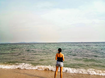 Rear view of man standing on beach against sky