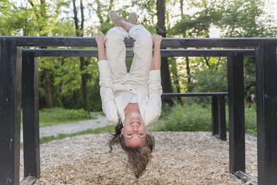 Full length portrait of woman hanging upside down on metallic bar at park