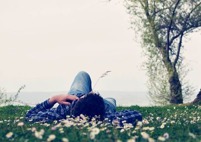 Mid adult man lying on grassy field against sky