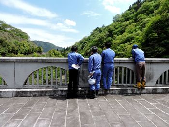 Rear view of engineers standing on bridge by railing against sky