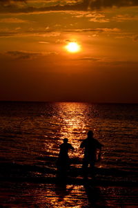 Silhouette people by sea against sky during sunset