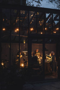 Male and female friends enjoying party in illuminated dining room at night