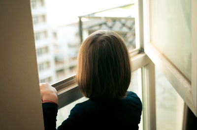 Rear view of woman looking through window at home