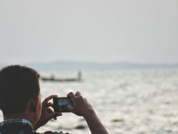 Rear view of man photographing sea from mobile phone