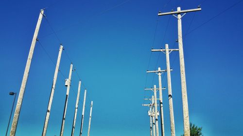 Low angle view of electricity pylon against clear blue sky