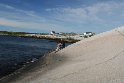 Man sitting on rock formation by sea at nova scotia