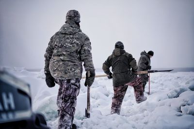 Rear view of people walking on snowcapped mountain during winter