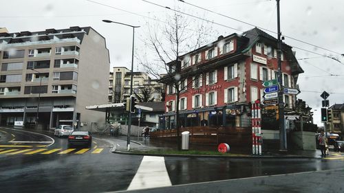 Cars on road by buildings in city during rainy season