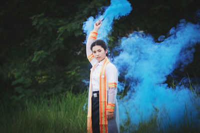 Portrait of woman holding distress flare while standing on field