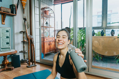 Portrait of smiling young woman holding drink bottle at home