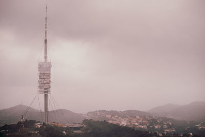 Communications tower in city against sky