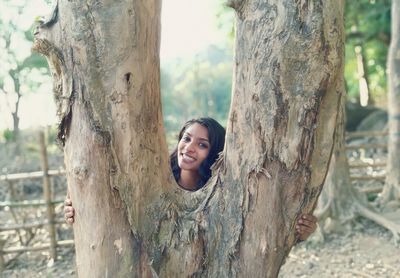 Portrait of smiling young woman against tree trunk