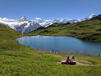 People sitting on lake by mountains against clear sky