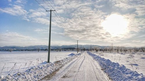 Snow covered railroad tracks on field against sky