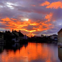 Scenic view of lake by buildings against sky during sunset