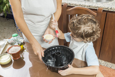 Midsection of mother preparing food with son at home