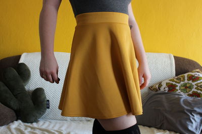 Midsection of woman wearing yellow skirt against sofa at home