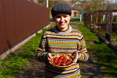 Ukrainian young smiling woman in hat holding plate of collection of red egg on nature background.