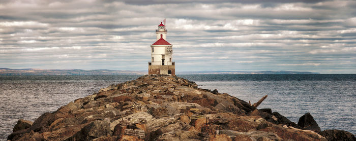 Lighthouse on rock by sea against sky