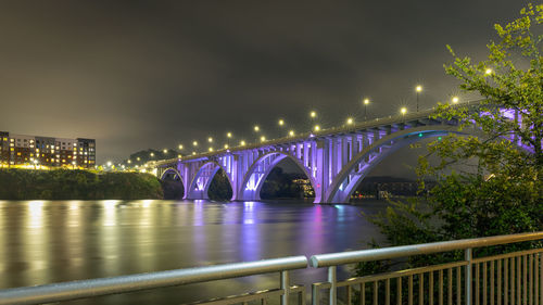 Illuminated bridge over river in city against sky at night