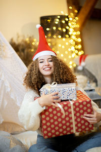 Pretty lady woman holding large christmas giftboxes in arms wear knitted pullover and santa hat 