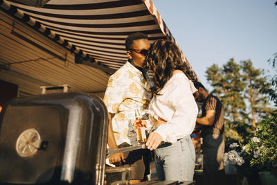 Girlfriend kissing boyfriend while standing by barbecue grill in party