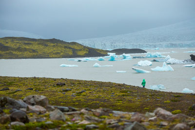 Rear view of woman by glaciers in sea against sky