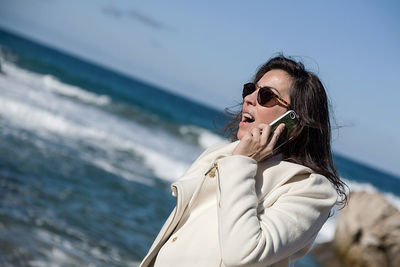 Woman talking on phone while standing at beach 