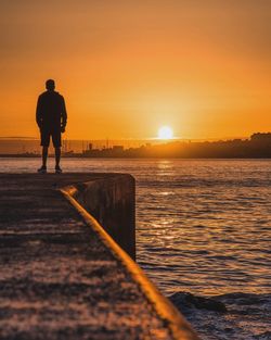 Rear view of silhouette man standing by sea against sky during sunset