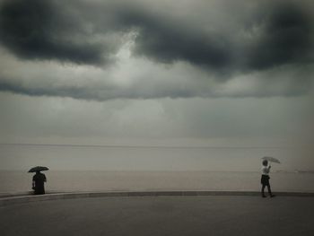 People on beach with umbrellas against cloudy sky during monsoon