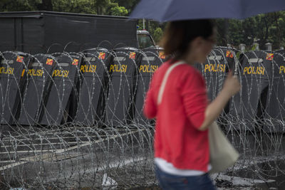 Woman holding umbrella while walking by barbed wire and riot shields on forbidden street