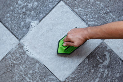 Using a green color plastic floor scrubber to scrub the tile floor with a floor cleaner.