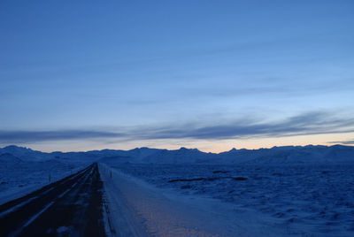 Road by railroad tracks against sky during winter