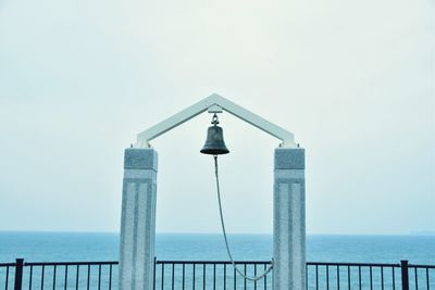 Bell hanging on structure by sea against clear sky