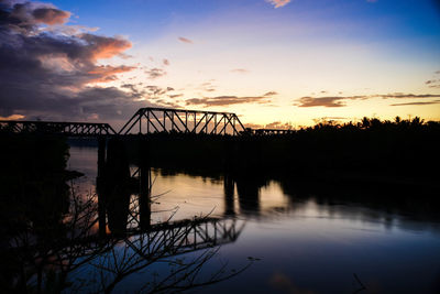 Silhouette of bridge over river during sunset