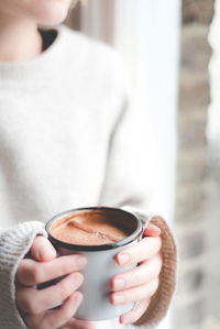 Midsection of mid adult woman holding coffee while standing by window at home