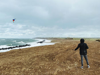 Rear view of man standing on beach against sky