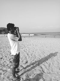 Rear view of man standing on beach against clear sky