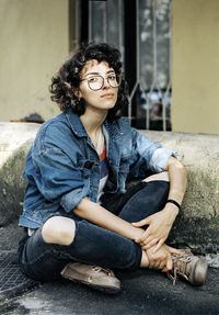 Curly haired woman in glasses sitting on the pavement near the house