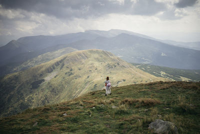 Rear view of woman walking on mountain against cloudy sky