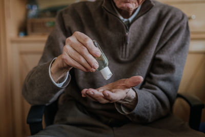Midsection of senior man using hand sanitizer at home
