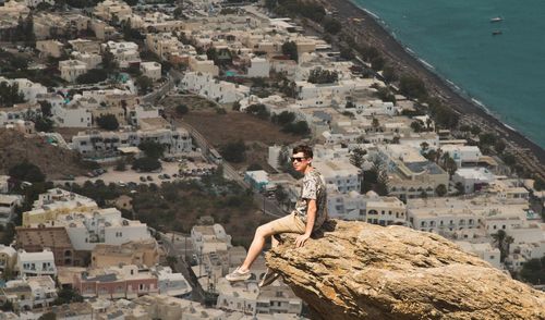View of man sitting on rock over view of a city
