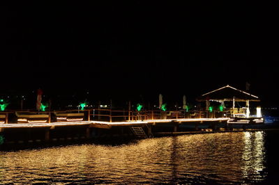 Illuminated pier by sea against clear sky at night