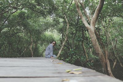 Woman sitting on pier amidst trees at forest