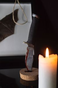 Close-up of illuminated candles by knife on table