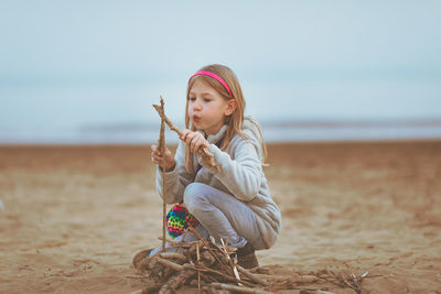 Girl playing with wood while kneeling at beach