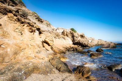 Rock formation in sea against clear blue sky